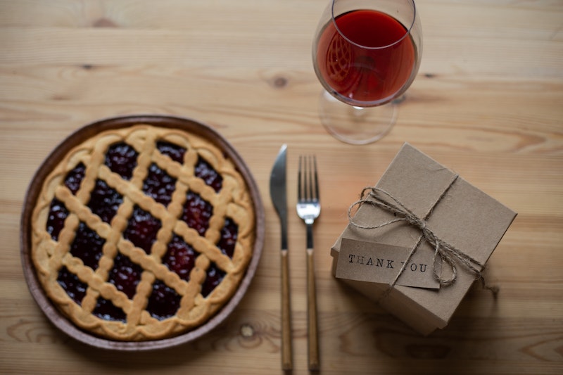 Delicious pie near glass of wine and gift box with thank you note on table